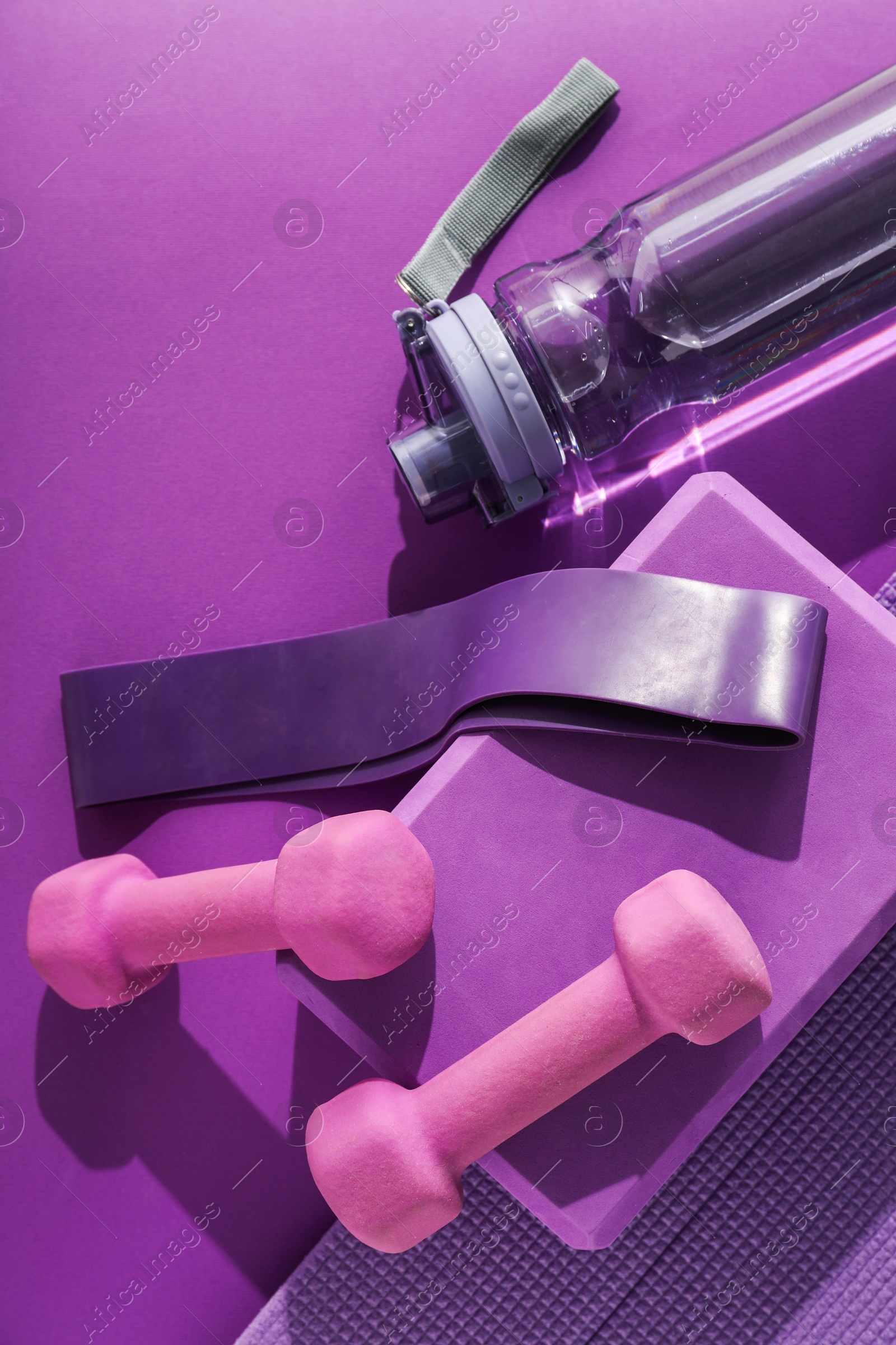 Photo of Dumbbells, yoga block, mat, fitness elastic band and bottle on purple background, flat lay