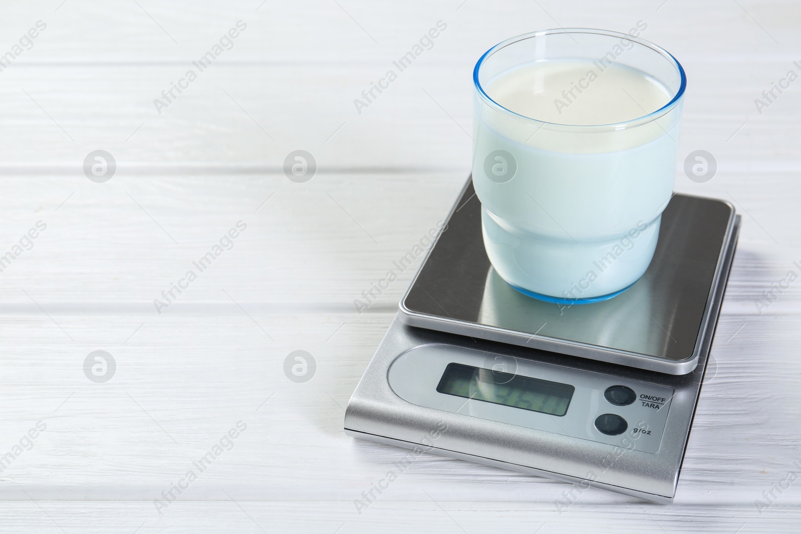 Photo of Kitchen scale with glass of milk on white wooden table, closeup. Space for text