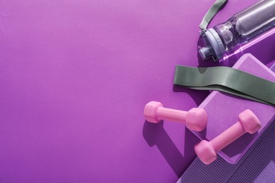 Dumbbells, yoga block, mat, fitness elastic band and bottle on purple background, flat lay. Space for text