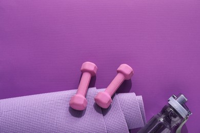 Dumbbells, yoga mat and bottle on purple background, flat lay. Space for text