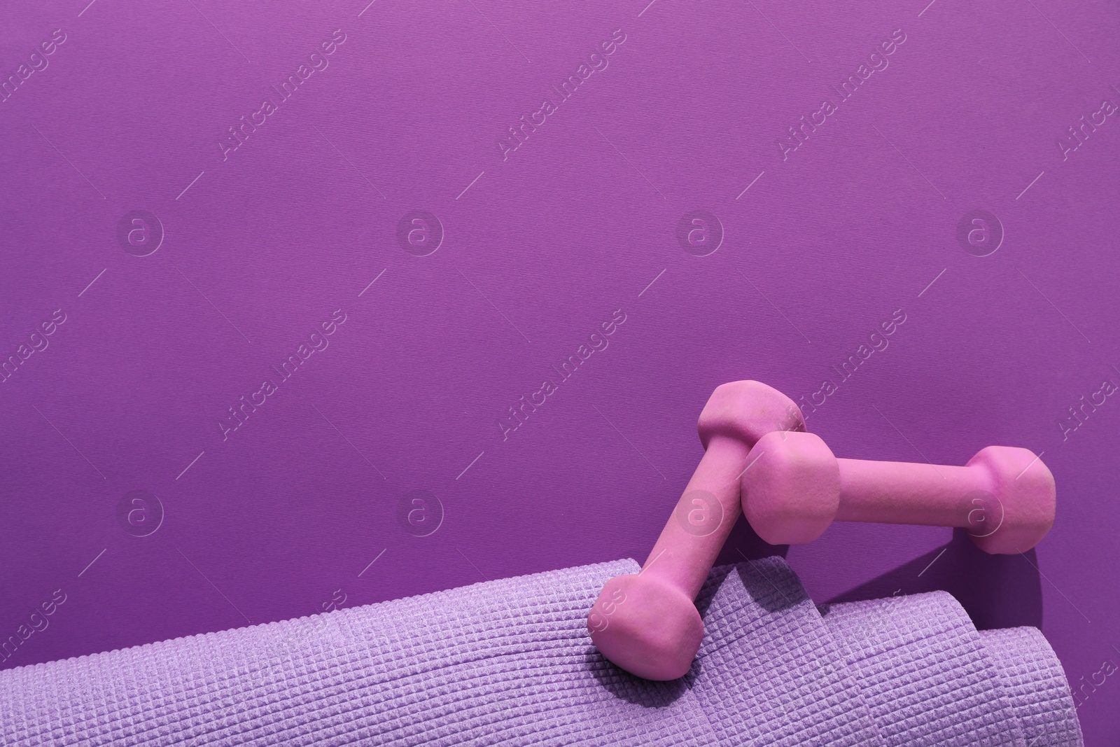 Photo of Dumbbells and yoga mat on purple background, flat lay. Space for text