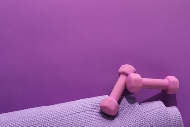 Dumbbells and yoga mat on purple background, flat lay. Space for text