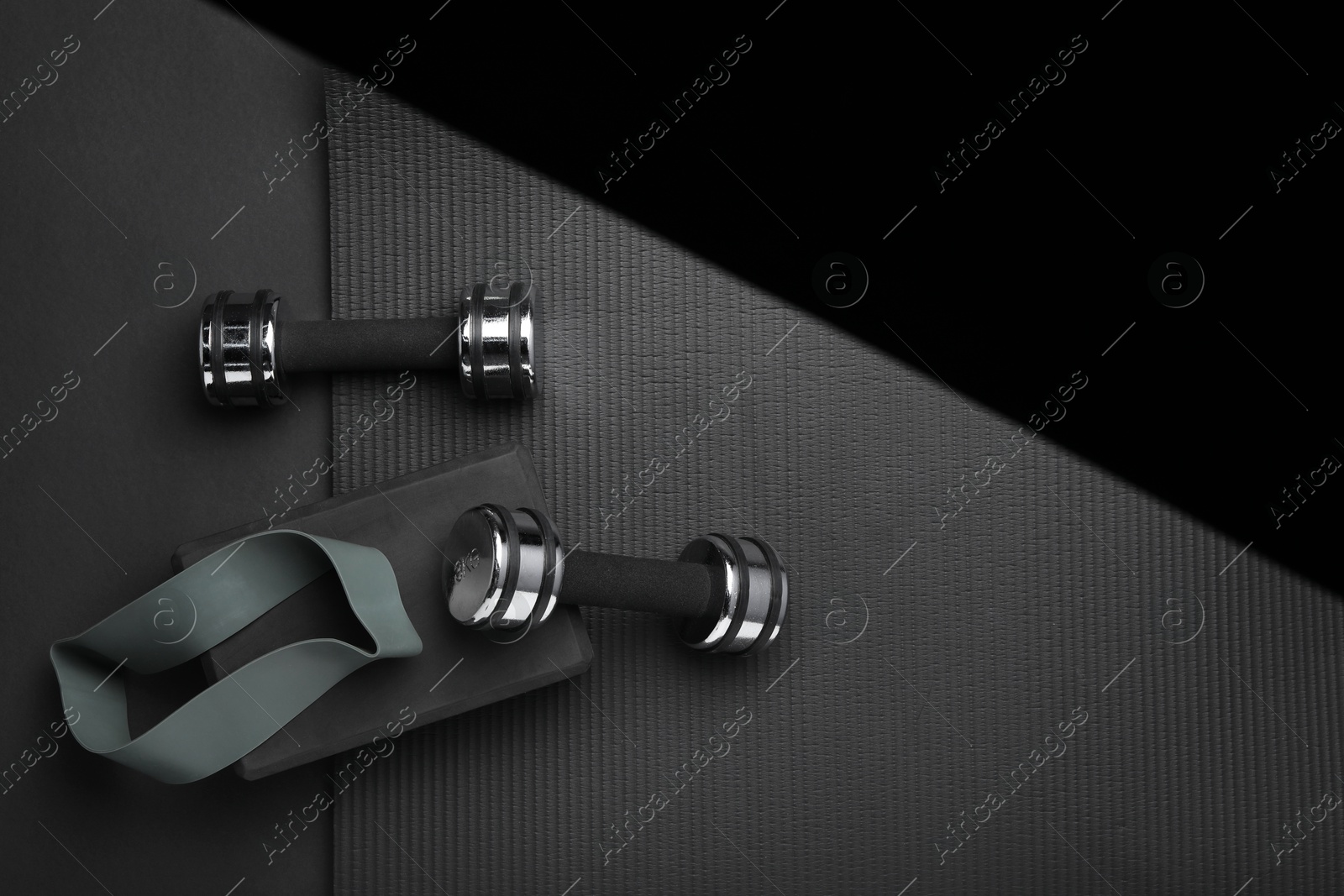 Photo of Dumbbells, yoga block, mat and fitness elastic band on black background, flat lay. Space for text