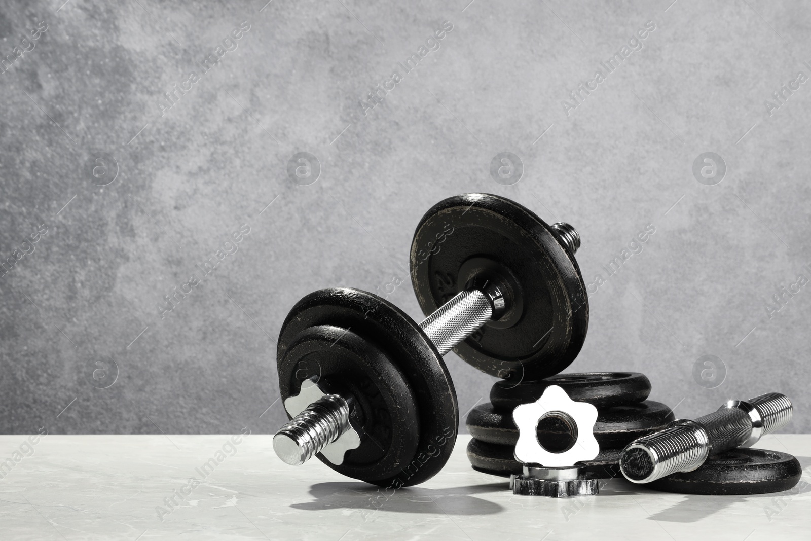 Photo of Barbell and parts of one on light table against grey background. Space for text