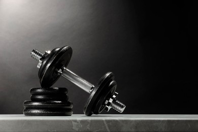 Barbell and stack of plates on marble table against dark background. Space for text