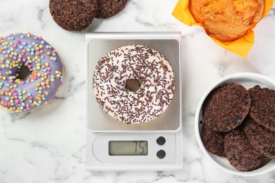 Flat lay composition of kitchen scale with donut on white marble table