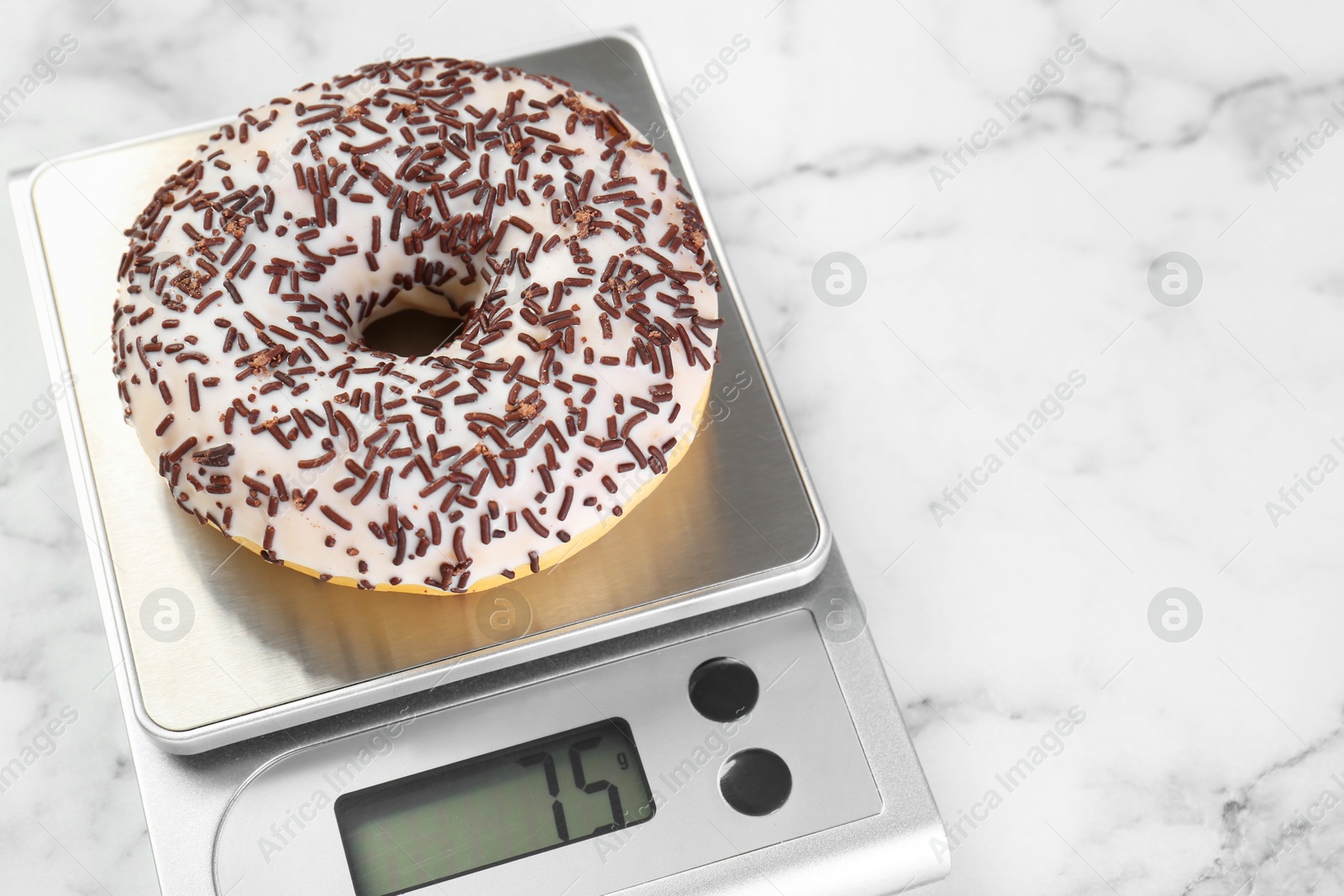 Photo of Kitchen scale with donut on white marble table, closeup. Space for text