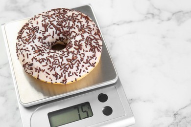 Photo of Kitchen scale with donut on white marble table, closeup. Space for text