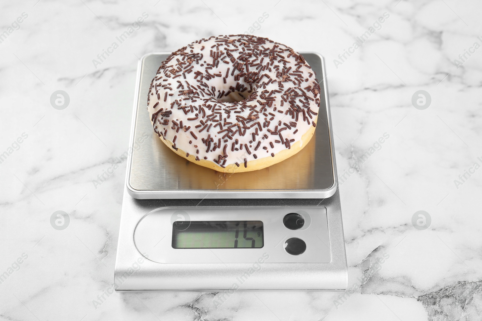 Photo of Kitchen scale with donut on white marble table, closeup