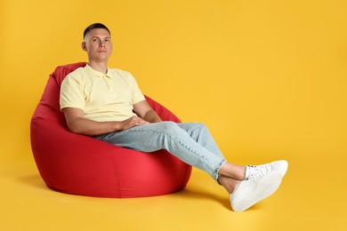 Photo of Handsome man resting on red bean bag chair against yellow background