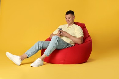 Photo of Handsome man with smartphone on red bean bag chair against yellow background