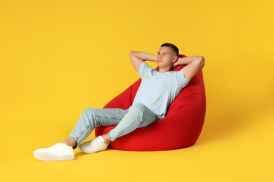 Photo of Handsome man resting on red bean bag chair against yellow background