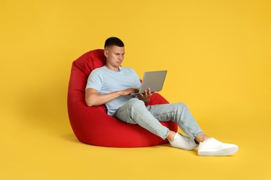 Photo of Handsome man with laptop on red bean bag chair against yellow background