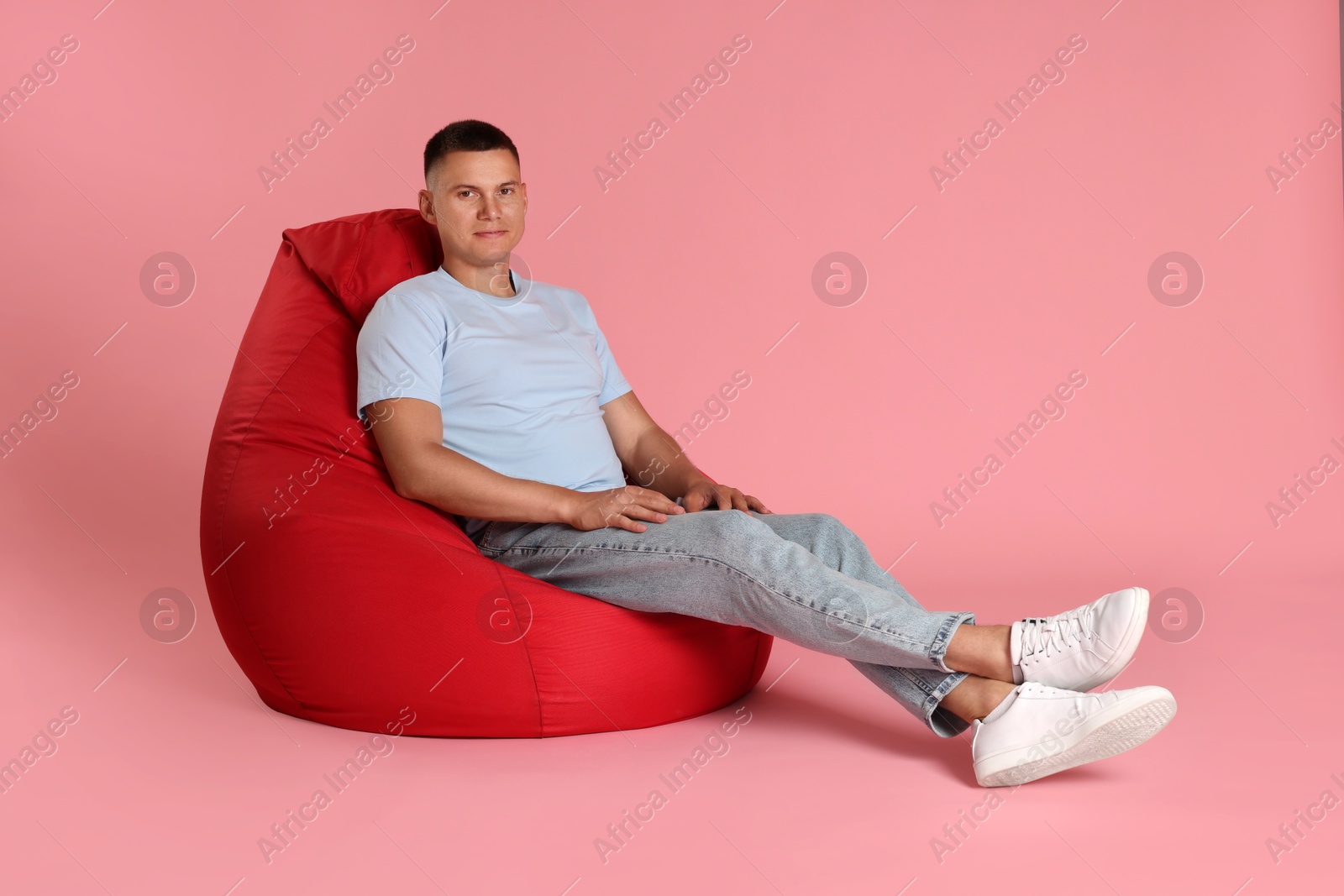 Photo of Handsome man on red bean bag chair against pink background