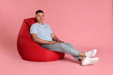 Handsome man on red bean bag chair against pink background