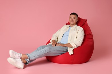 Handsome man on red bean bag chair against pink background