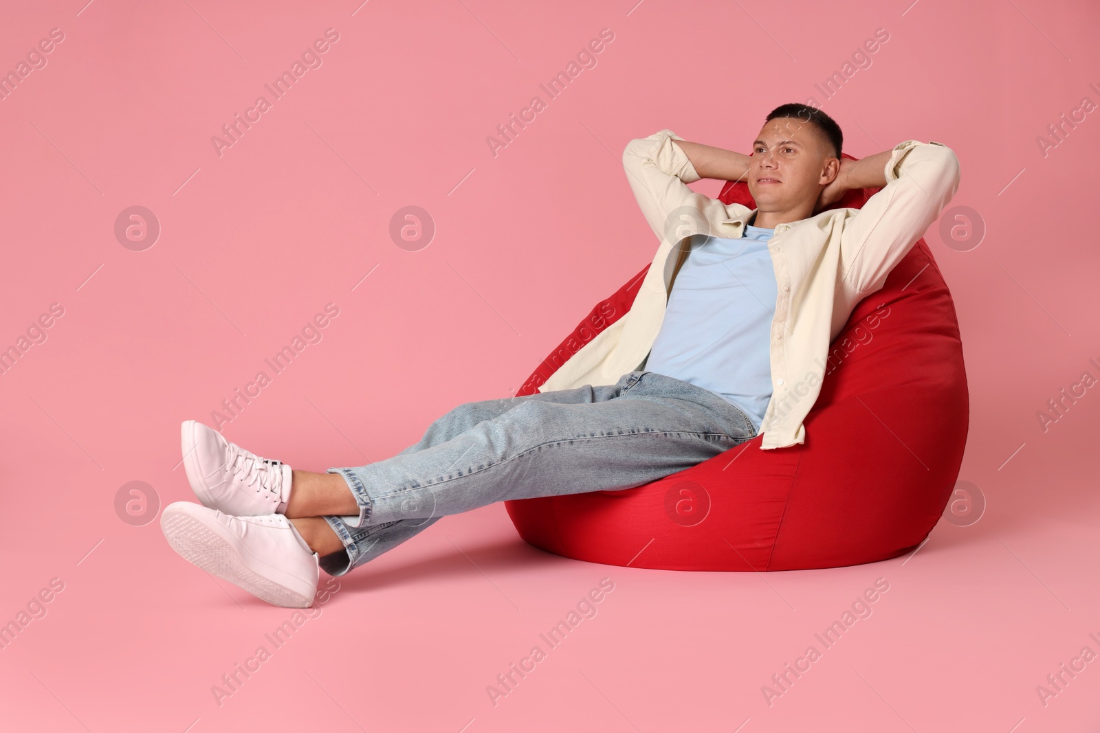 Photo of Handsome man on red bean bag chair against pink background