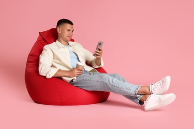 Photo of Handsome man with smartphone on red bean bag chair against pink background