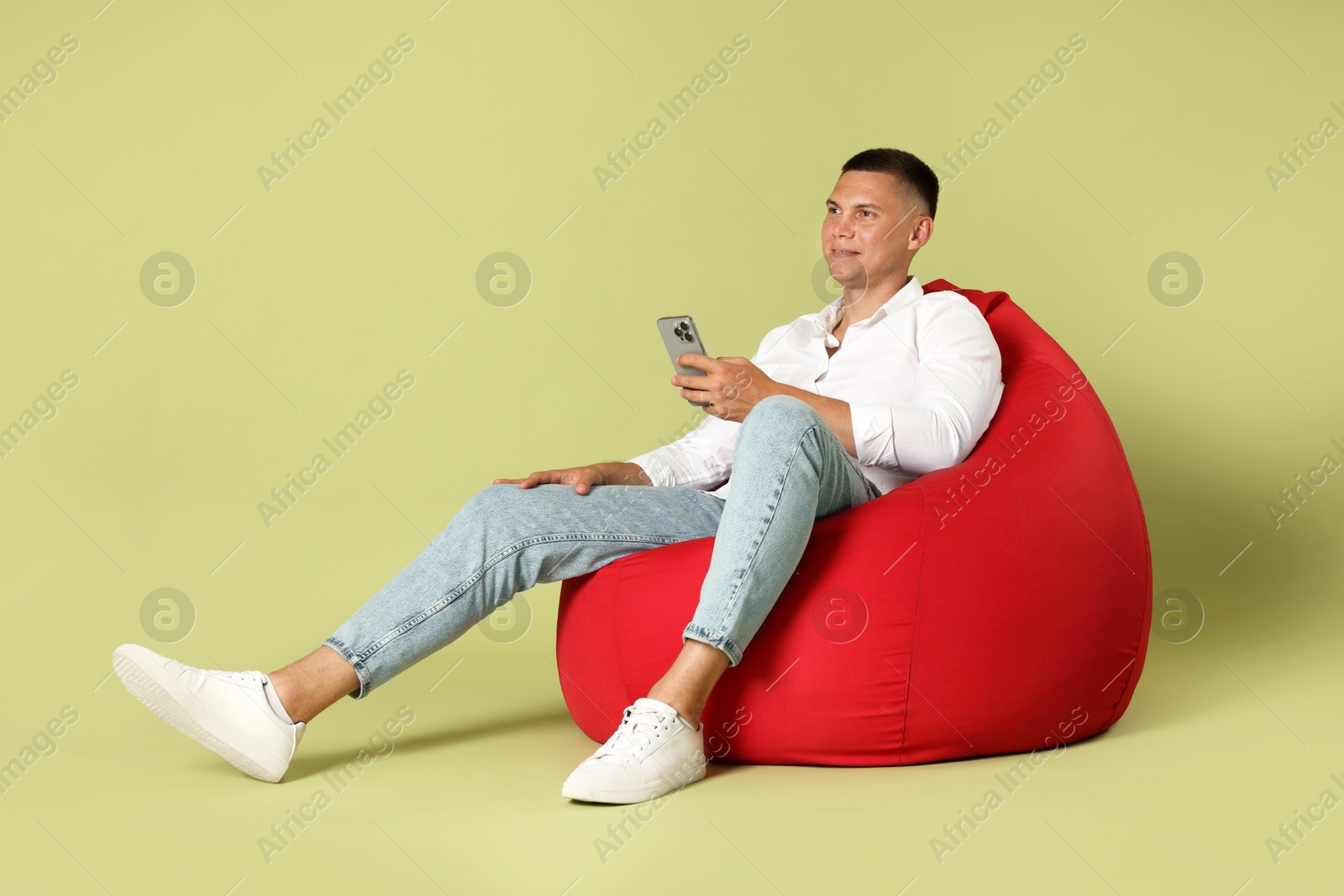 Photo of Handsome man with smartphone on red bean bag chair against green background