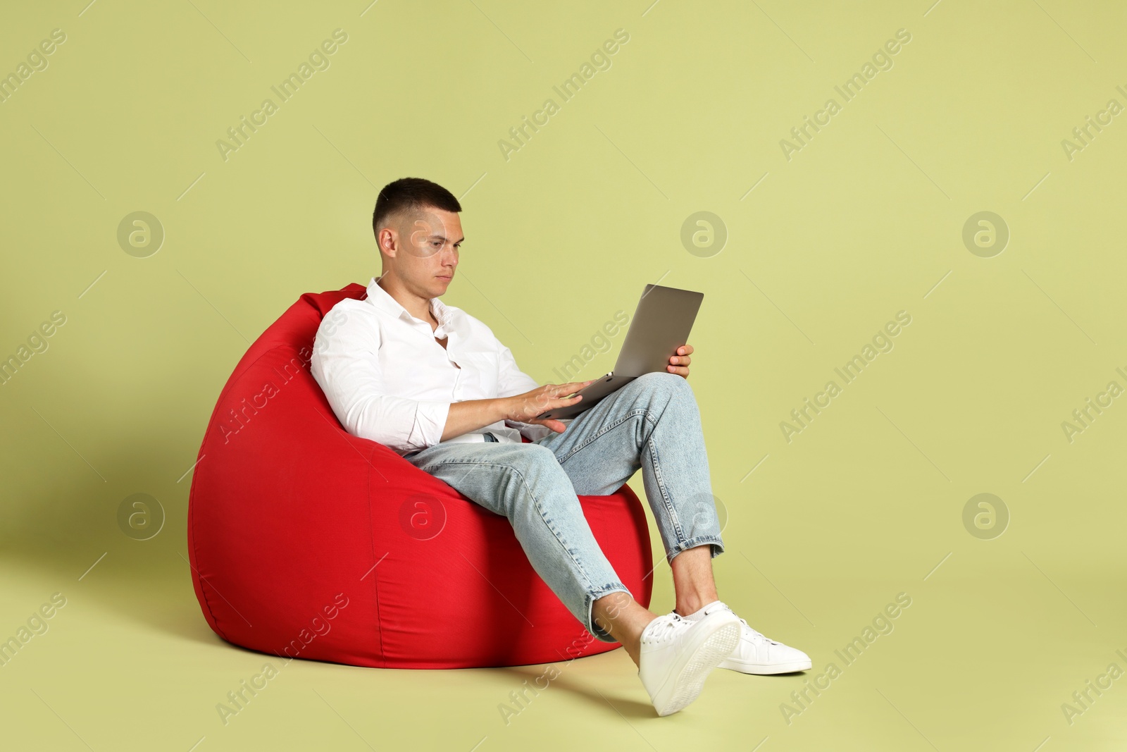 Photo of Handsome man with laptop on red bean bag chair against green background