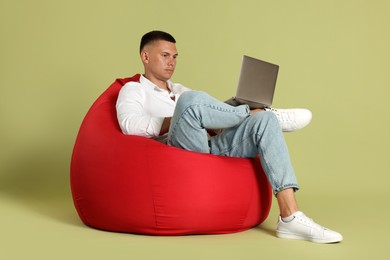 Handsome man with laptop on red bean bag chair against green background