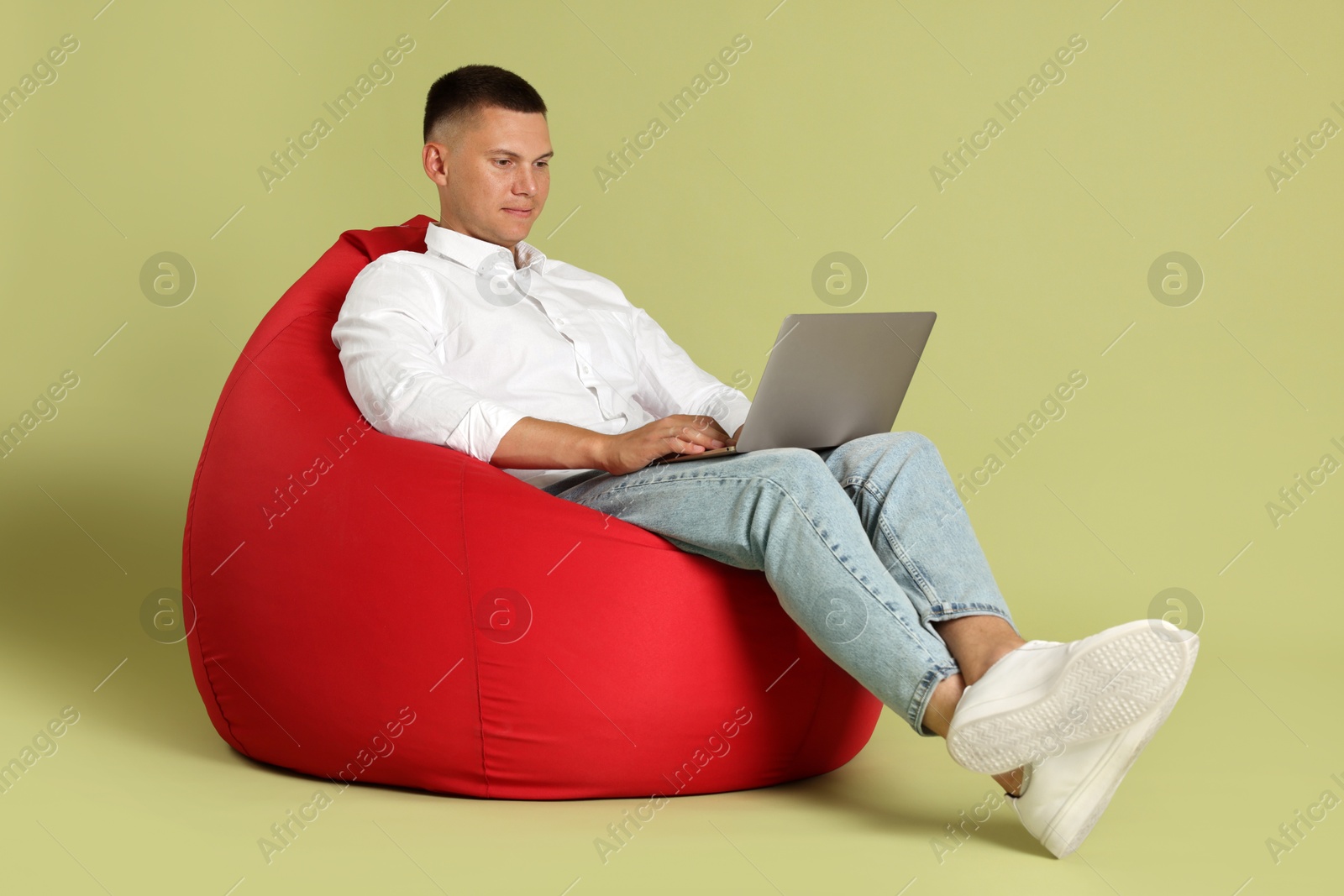 Photo of Handsome man with laptop on red bean bag chair against green background