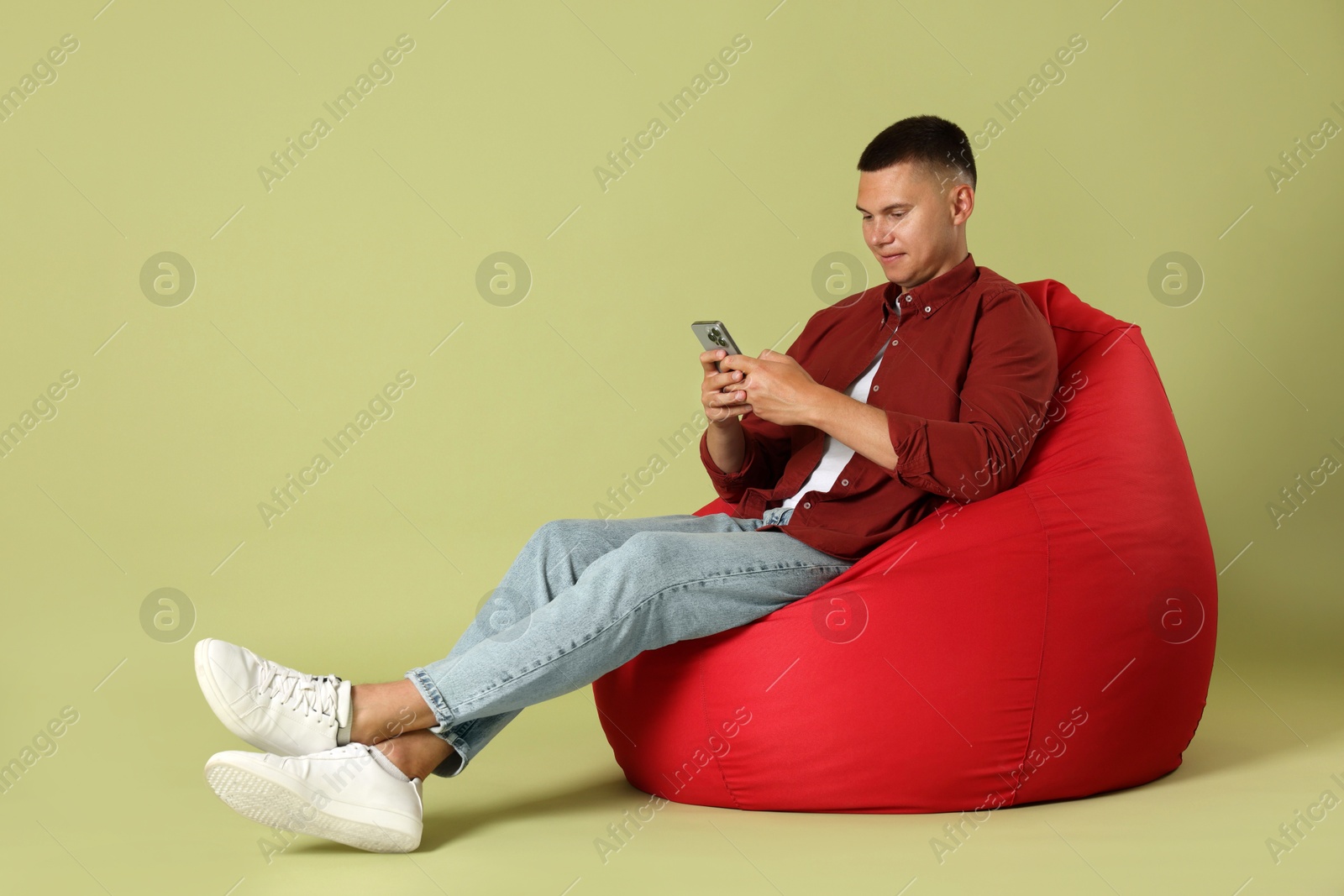 Photo of Handsome man with smartphone on red bean bag chair against green background