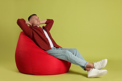 Photo of Handsome man resting on red bean bag chair against green background
