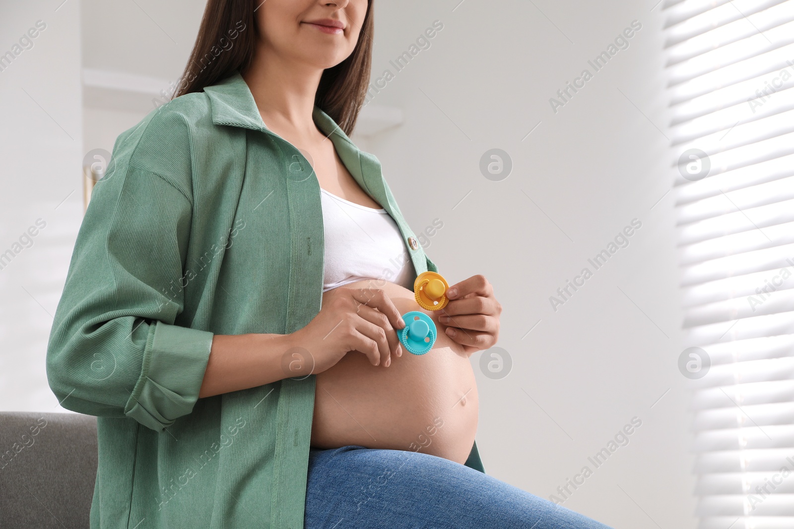 Photo of Pregnant woman with pacifiers at home, closeup. Expecting twins