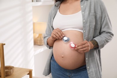 Photo of Pregnant woman with pacifiers at home, closeup. Expecting twins