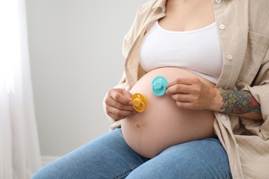 Pregnant woman with pacifiers at home, closeup and space for text. Expecting twins