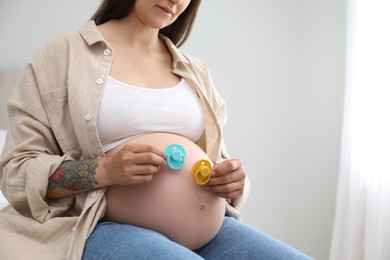 Pregnant woman with pacifiers at home, closeup and space for text. Expecting twins