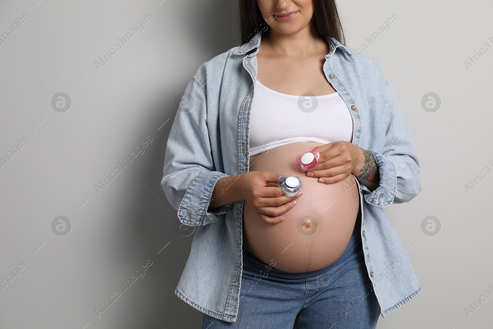 Photo of Pregnant woman with pacifiers on light gray background, closeup and space for text. Expecting twins