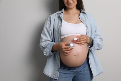 Pregnant woman with pacifiers on light gray background, closeup and space for text. Expecting twins