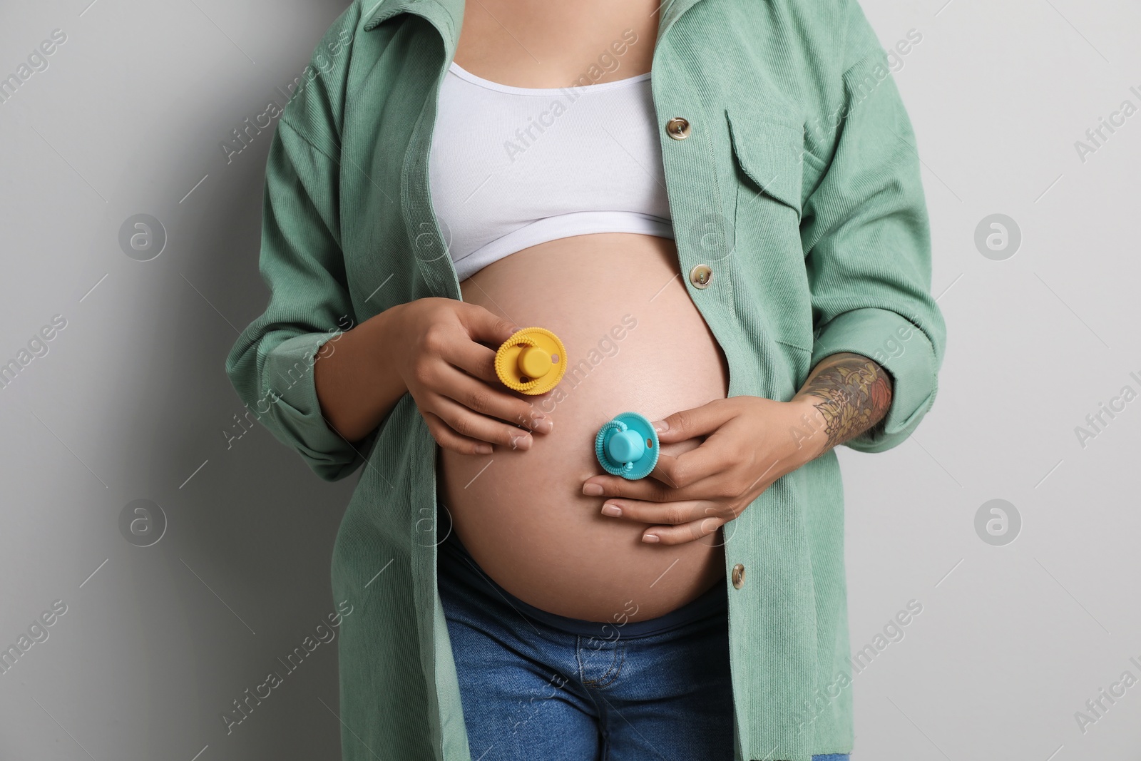 Photo of Pregnant woman with pacifiers on light gray background, closeup. Expecting twins