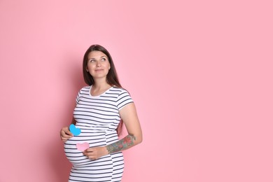 Beautiful pregnant woman with paper hearts on pink background, space for text. Expecting twins