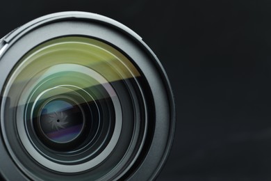 Modern camera lens on black table, closeup. Space for text