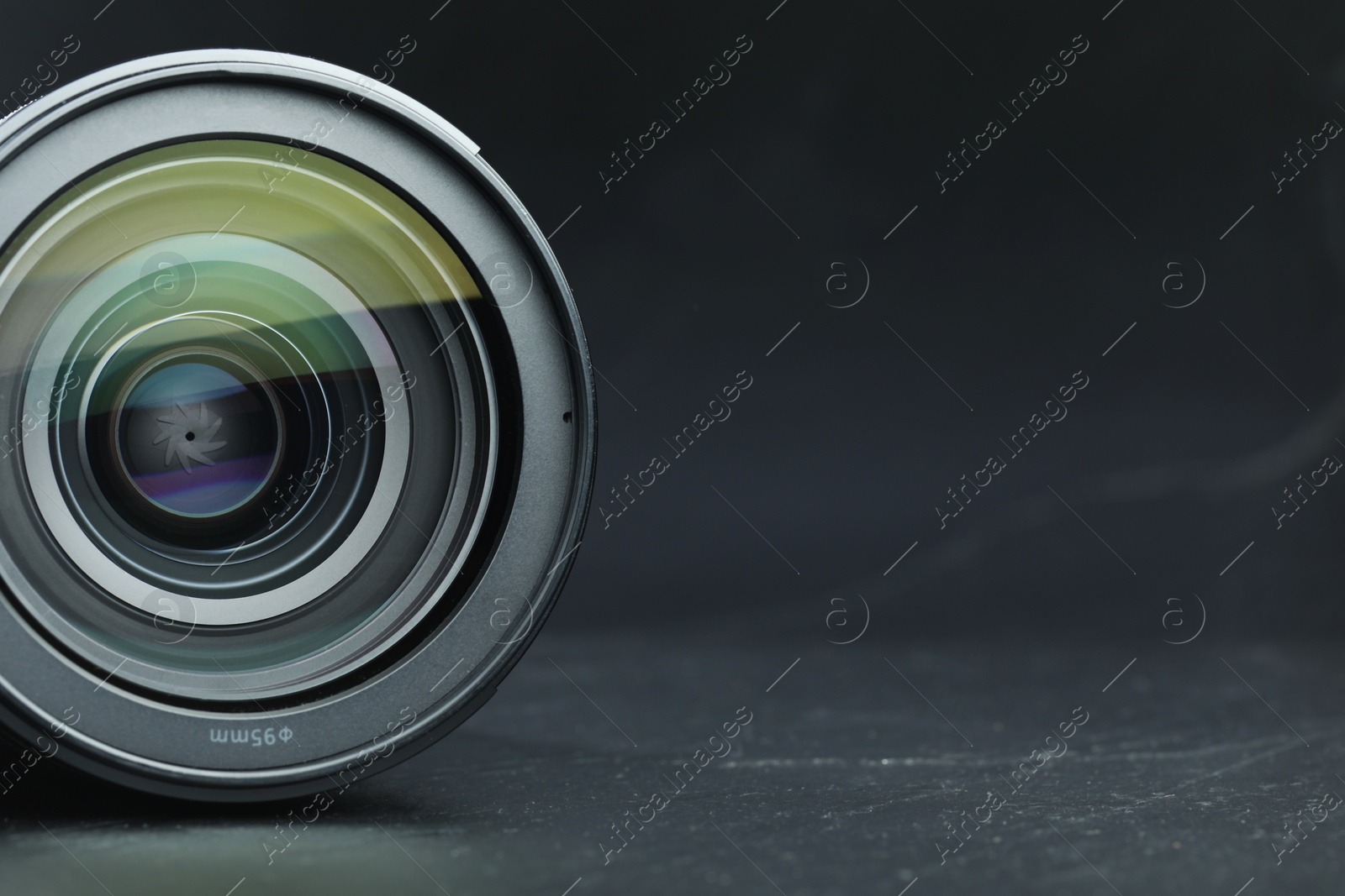 Photo of Modern camera lens on black table, closeup. Space for text