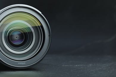 Photo of Modern camera lens on black table, closeup. Space for text