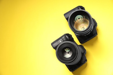 Photo of Two modern photo cameras on yellow background, top view. Space for text