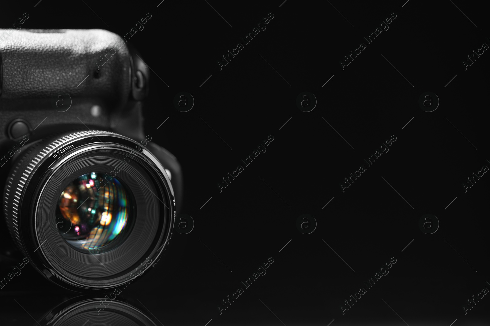 Photo of Modern photo camera on black mirror surface, space for text