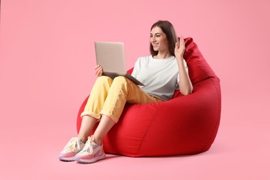 Photo of Smiling woman with laptop having online meeting on red bean bag chair against pink background