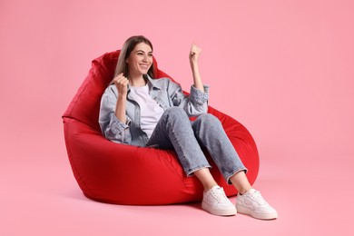 Photo of Smiling woman sitting on red bean bag chair against pink background