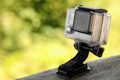 Photo of Modern action camera with mount on wooden surface outdoors, closeup. Space for text