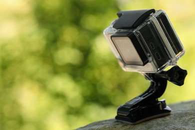 Photo of Modern action camera with mount on wooden surface outdoors, closeup. Space for text