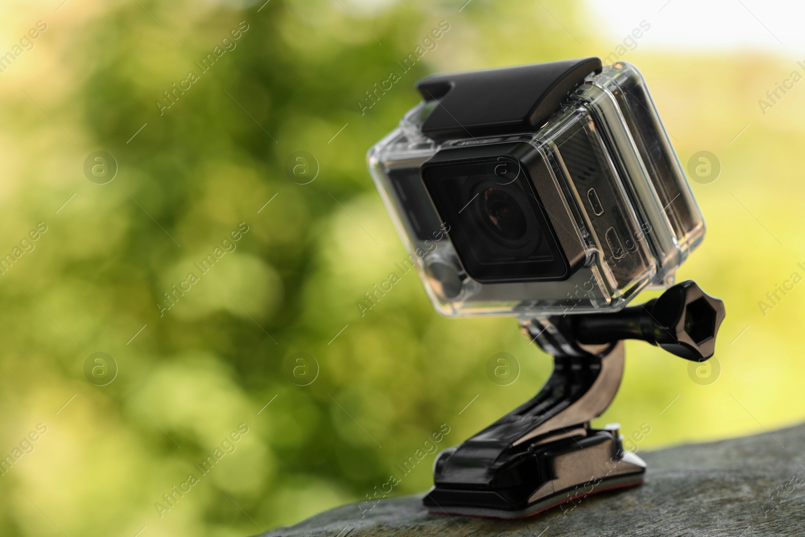 Photo of Modern action camera with mount on wooden surface outdoors, closeup. Space for text