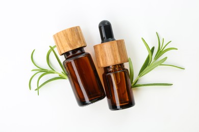 Photo of Aromatic essential oils in bottles and rosemary on white background, flat lay