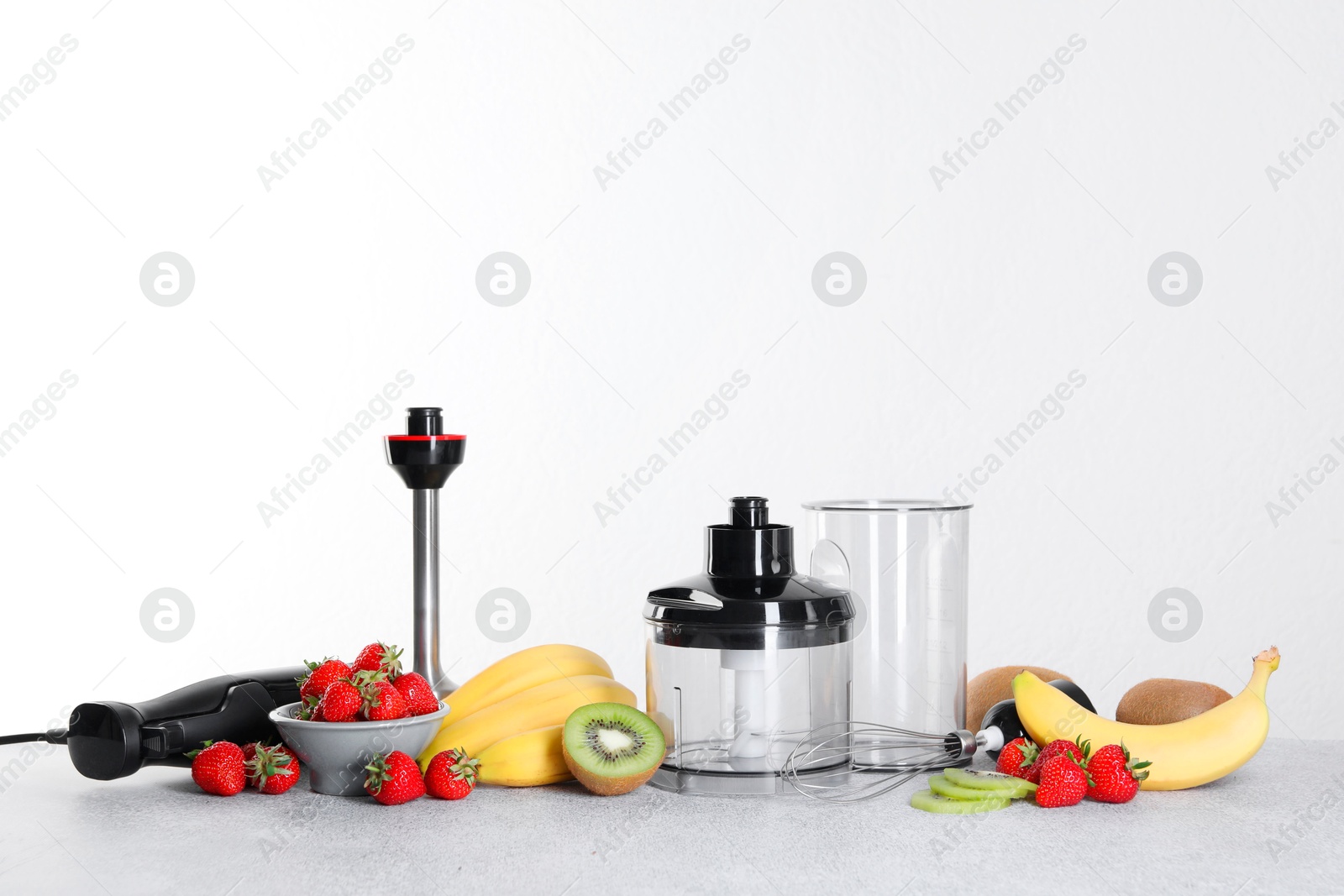 Photo of Hand blender kit, fresh fruits and strawberries on gray table against white background, space for text