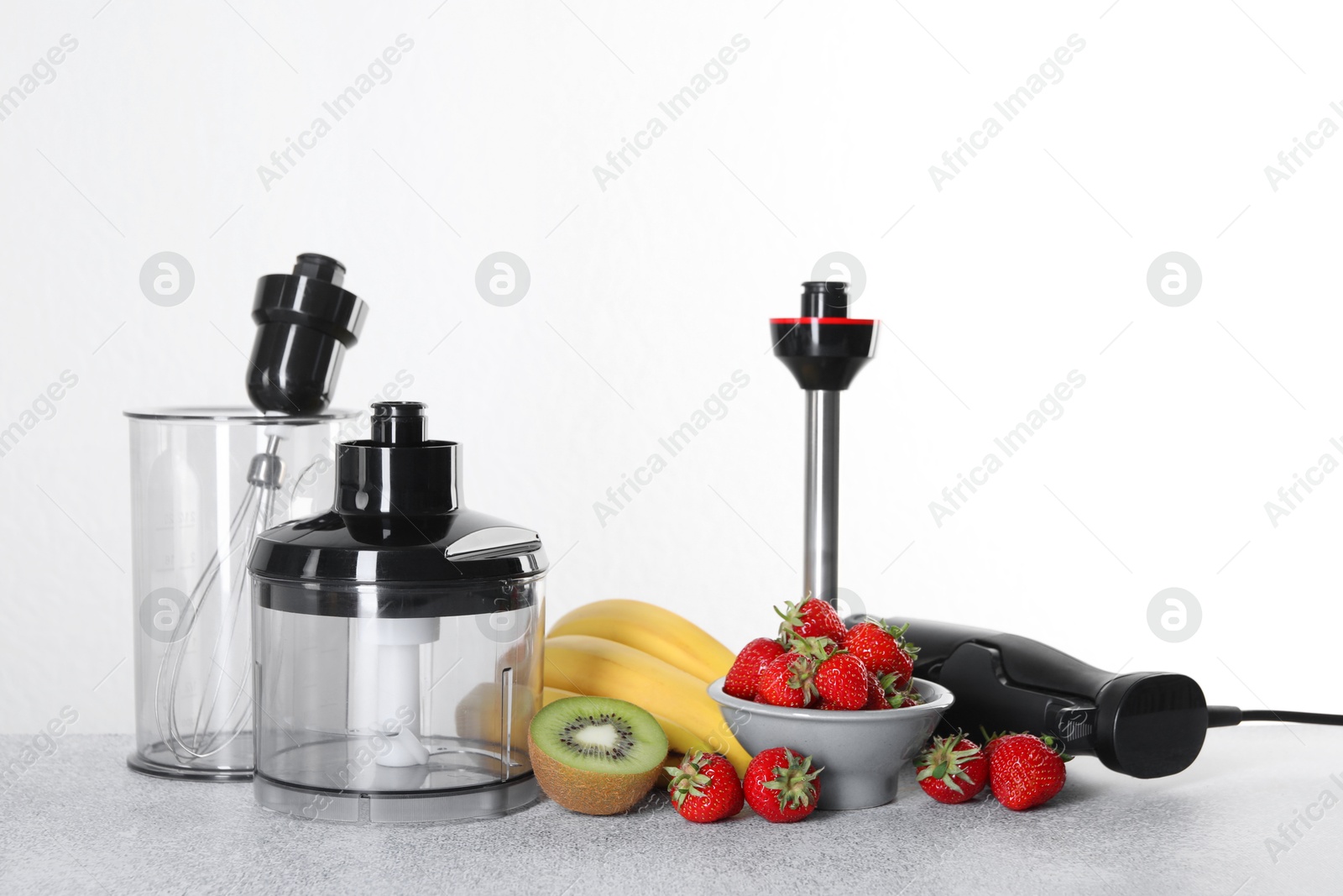 Photo of Hand blender kit, fresh fruits and strawberries on gray table against white background