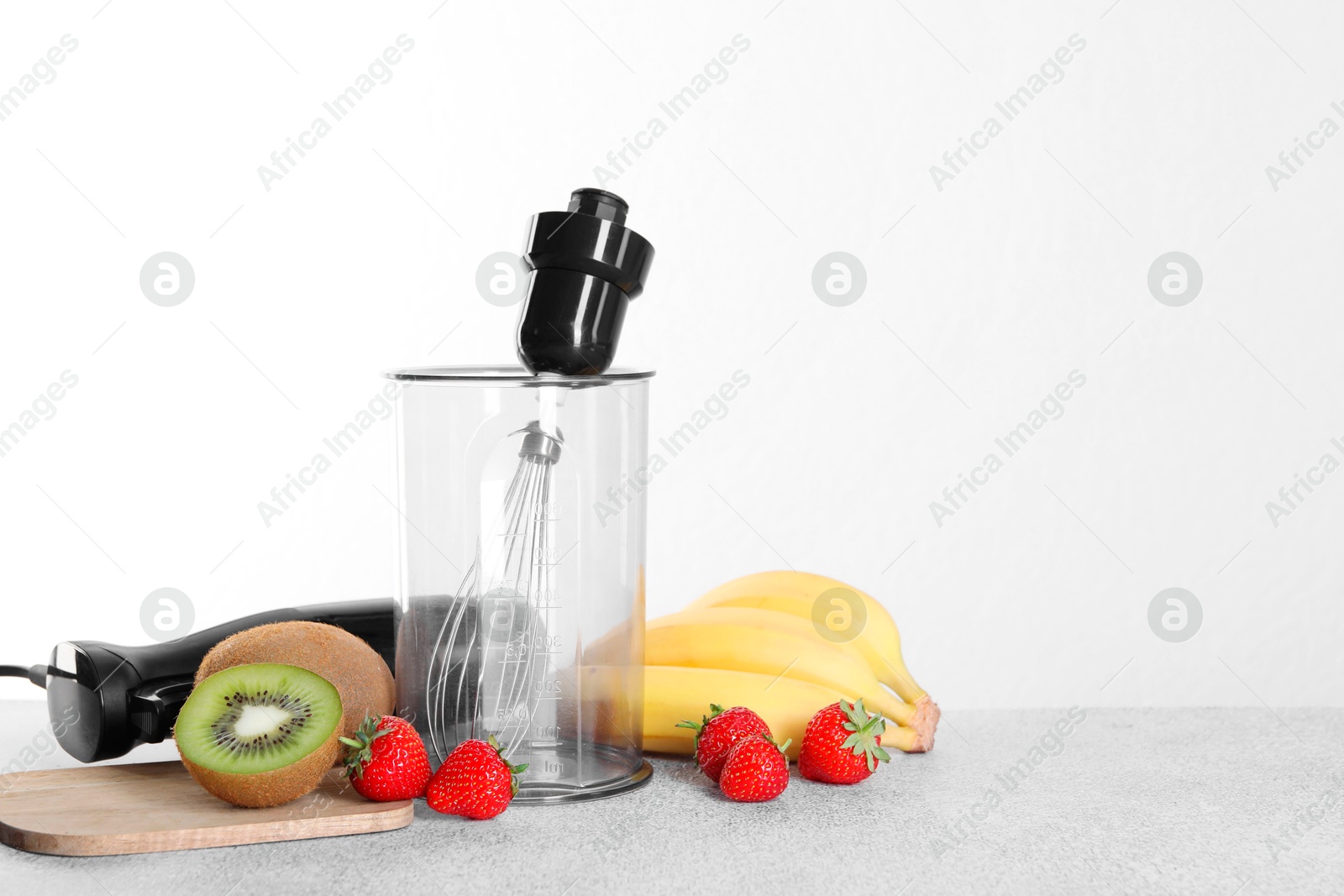 Photo of Hand blender kit, fresh fruits and strawberries on gray table against white background, space for text